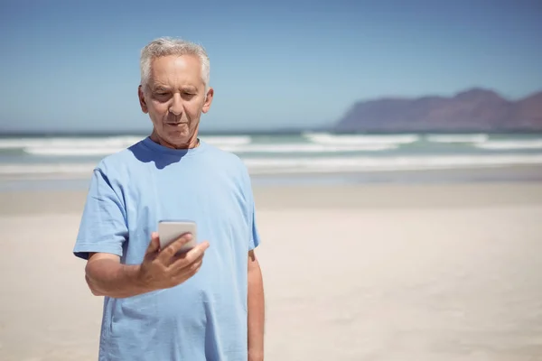 Starszy człowiek posiadający telefon na plaży — Zdjęcie stockowe