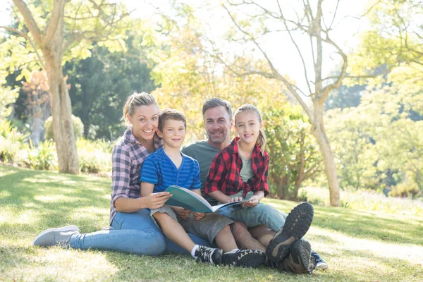Family reading a book in park — Stock Photo, Image