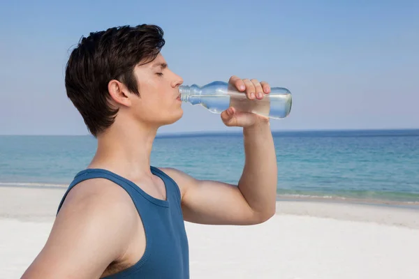 Homme eau potable de la bouteille à la plage — Photo