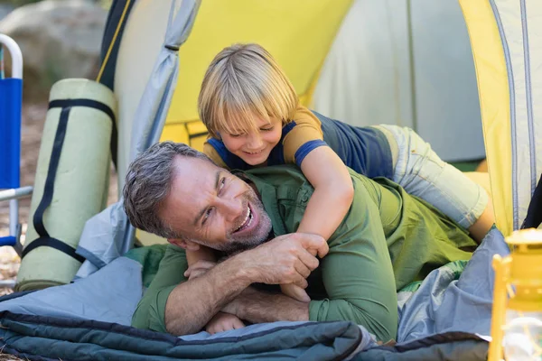 Menino brincalhão deitado no pai na tenda — Fotografia de Stock