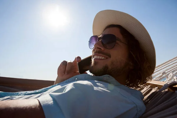 Людина розслабляється на гамаку і розмовляє по телефону — стокове фото