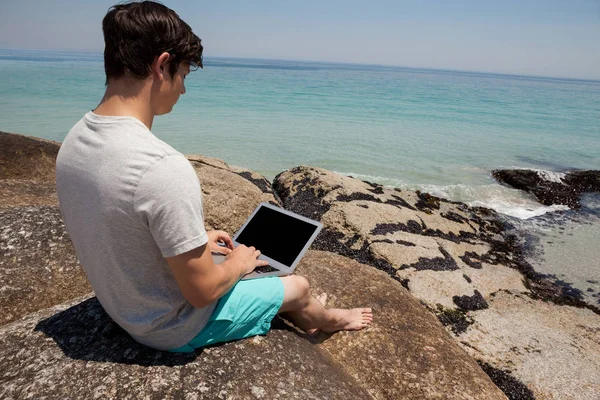 Homem em rochas e usando laptop na costa do mar — Fotografia de Stock