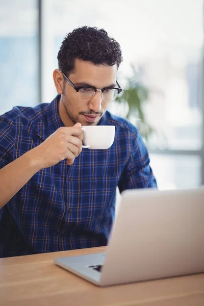Executive having coffee while using laptop — Stock Photo, Image