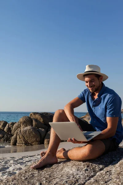 Man op de rotsen en het gebruik van laptop op strand — Stockfoto