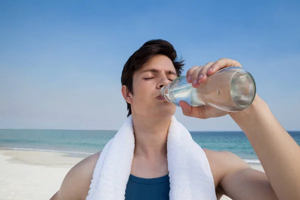 Homme eau potable de la bouteille à la plage — Photo