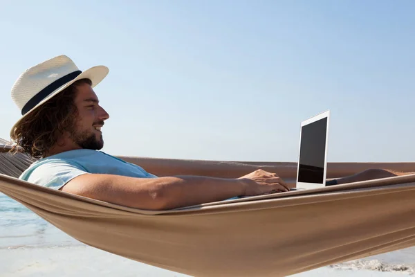 Uomo che usa il computer portatile mentre si rilassa sul hammock — Foto Stock