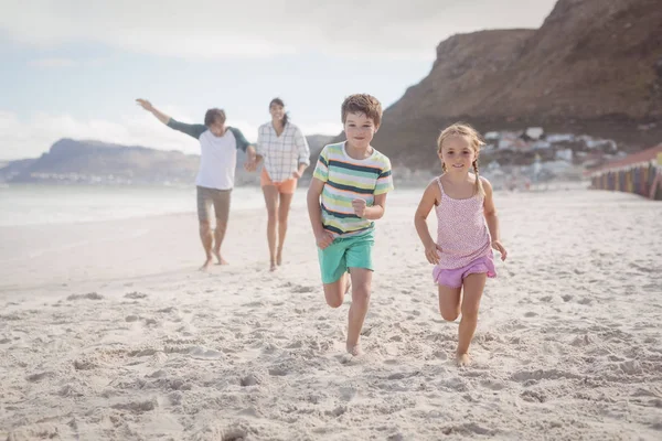 Братья и сёстры бегают по песку с родителями — стоковое фото