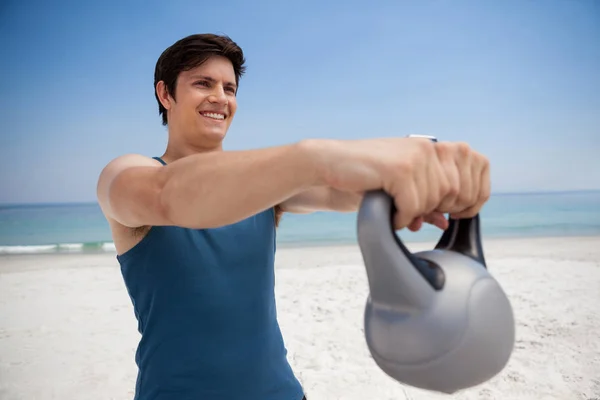 Hombre sosteniendo kettlebell en la playa — Foto de Stock