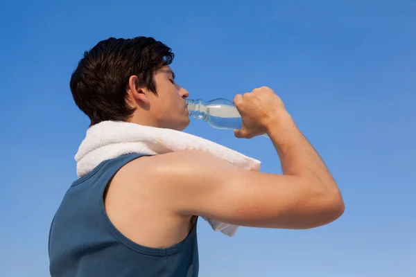 Человек пьет воду из бутылки на фоне голубого неба — стоковое фото