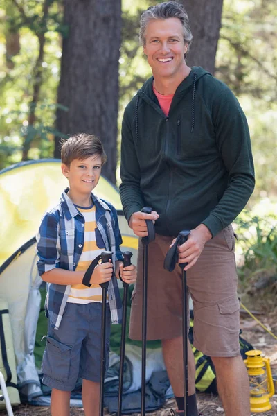 Father and son holding hiking poles in forest — Stock Photo, Image