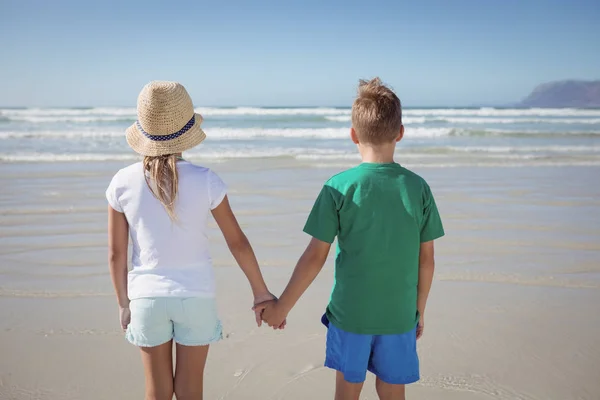 Rodzeństwo, trzymając się za ręce na brzegu plaży — Zdjęcie stockowe