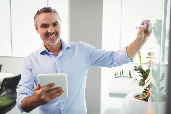 Executivo usando tablet enquanto escreve no quadro branco — Fotografia de Stock