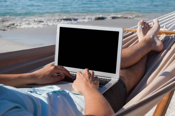 Homem usando laptop enquanto relaxa na rede — Fotografia de Stock