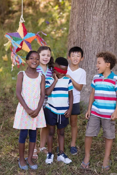 Friends standing with blindfolded boy on grassy field — Stock Photo, Image