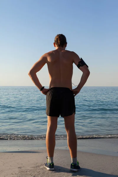 Muskulöser Mann, der vom Strand auf das Meer blickt — Stockfoto