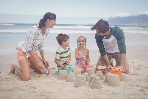 Irmãos com pais fazendo castelo de areia — Fotografia de Stock