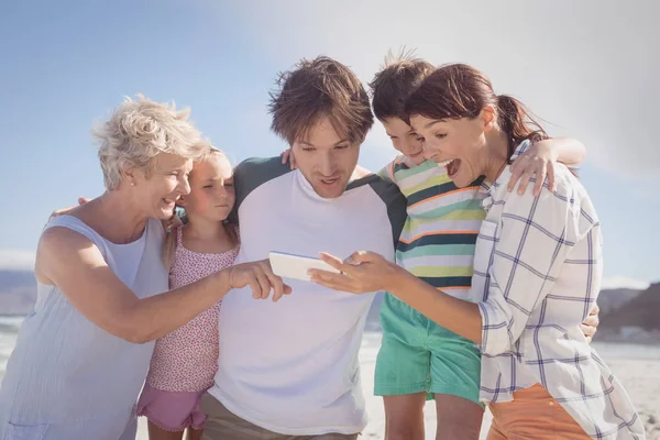 Familia usando el teléfono móvil en la playa — Foto de Stock