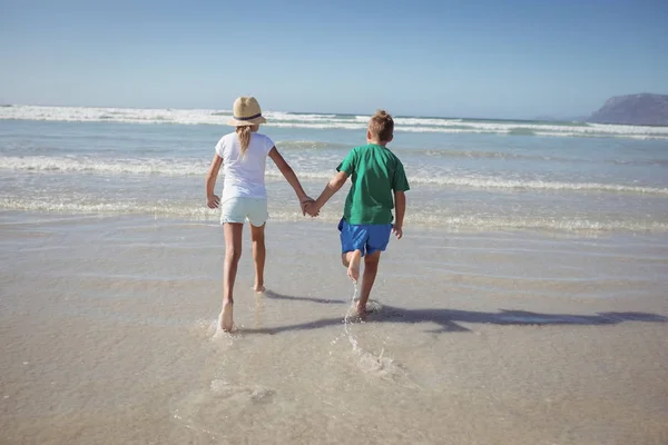 Siblings holding hands while running on shore — Stock Photo, Image