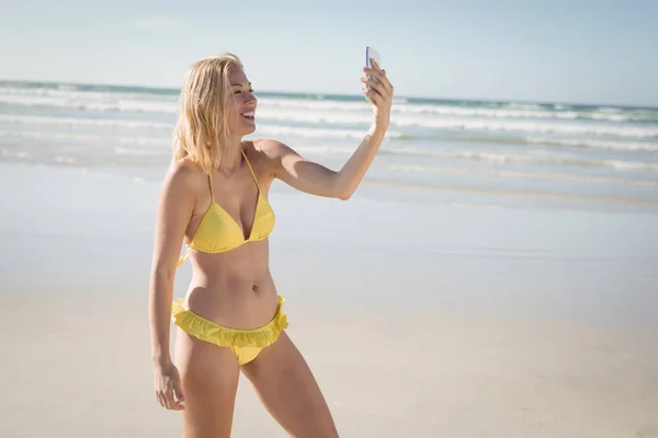 Женщина в жёлтом бикини делает селфи на пляже — стоковое фото
