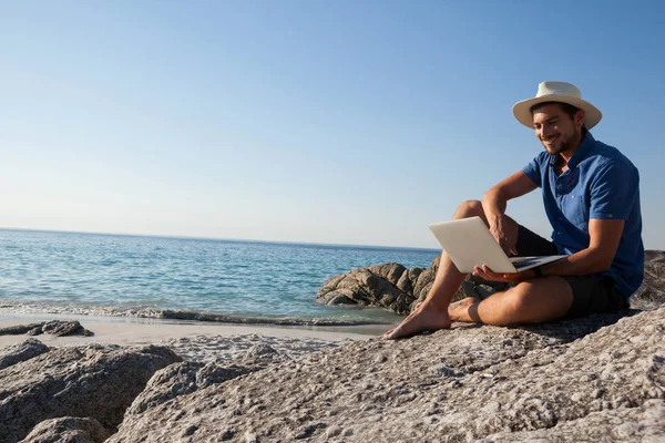 Człowiek na skały i komputera przenośnego na plaży — Zdjęcie stockowe