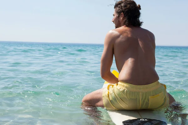 Surfista sentado en la tabla de surf en la costa —  Fotos de Stock