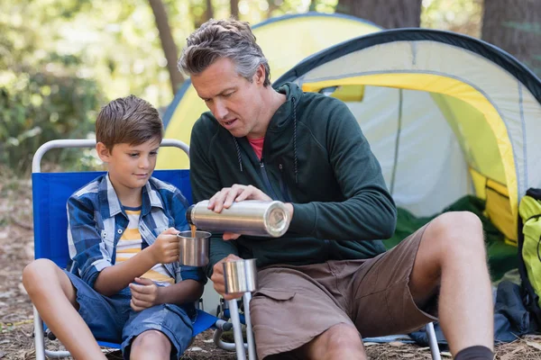 Father pouring drink in cup for son in forest — Stock Photo, Image