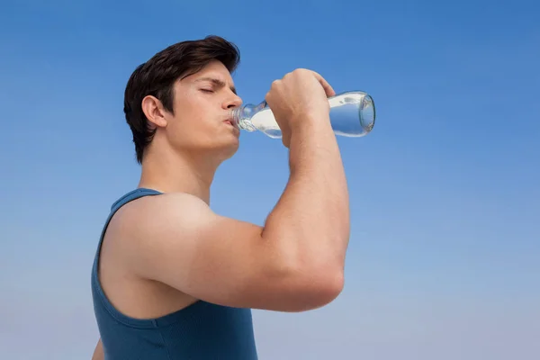 Muž pitnou vodu z láhve na pláži — Stock fotografie