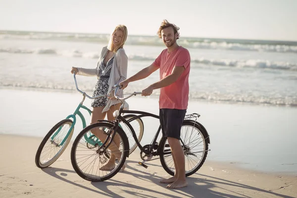 Casal com bicicletas de pé na praia — Fotografia de Stock