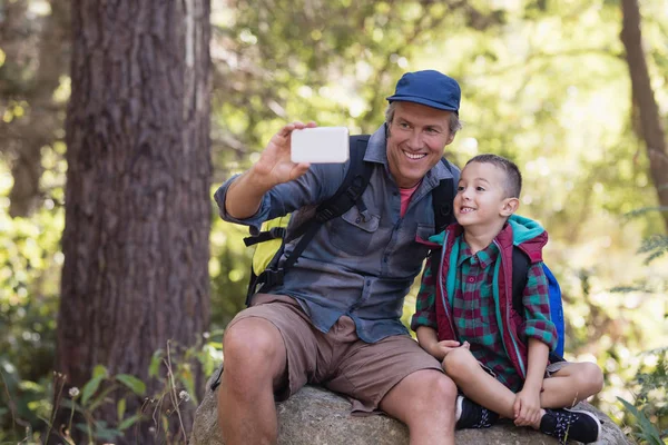 Vater sitzt mit Junge auf Felsen und macht Selfie — Stockfoto