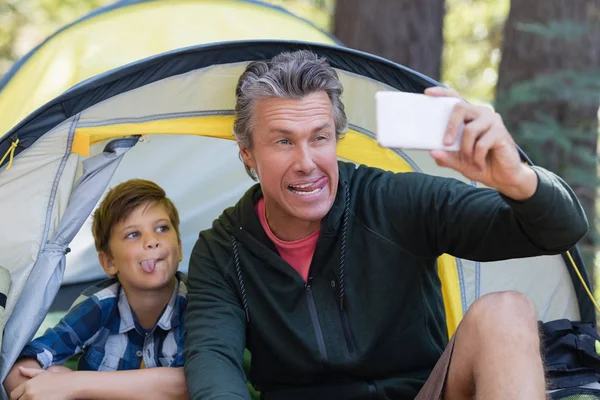 Игривый отец и сын делают селфи в палатке — стоковое фото