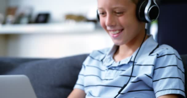 Хлопчик з навушниками, використовуючи ноутбук у вітальні — стокове відео
