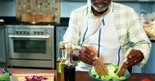 Pareja mayor preparando ensalada en la cocina — Vídeo de stock