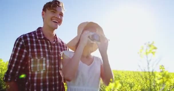 Casal tirando fotos da câmera no campo de mostarda — Vídeo de Stock