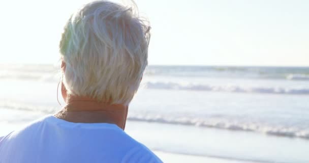 Старший чоловік слухає музику на навушниках на пляжі — стокове відео