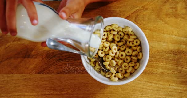 Händerna på kid hälla mjölk i spannmål skål — Stockvideo
