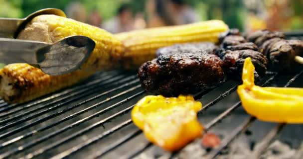 Чоловік смажить кукурудзу, м'ясо та овочі на барбекю — стокове відео