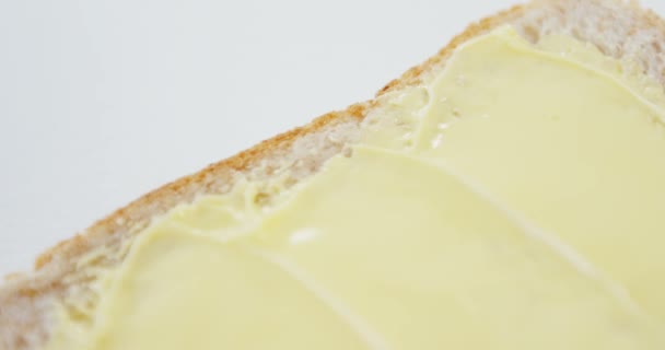 Boter verspreid over sneetje brood tegen witte achtergrond — Stockvideo