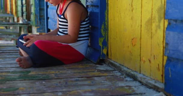 Fille en utilisant une tablette numérique près de la cabane de plage colorée — Video