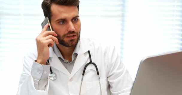 Чоловік лікар розмовляє на мобільному телефоні під час роботи на комп'ютері — стокове відео