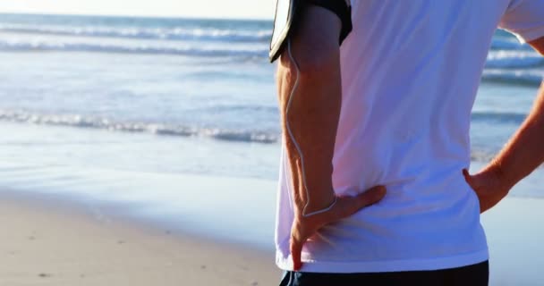 Homem sênior ouvindo música em fones de ouvido na praia — Vídeo de Stock