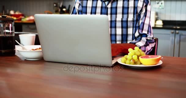 Hombre mayor sonriente usando el ordenador portátil mientras desayuna — Vídeo de stock
