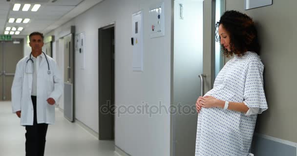Вагітна жінка торкається її живота, поки лікар ходить в коридорі — стокове відео