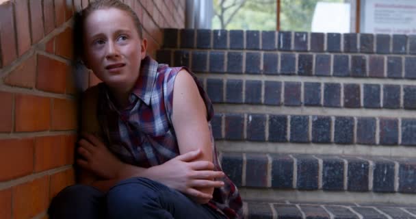 Sad schoolgirl sitting alone on staircase — Stock Video
