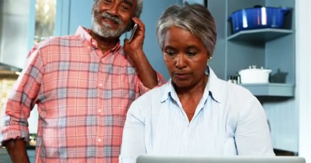 Senior couple using mobile phone and laptop in kitchen — Stock Video