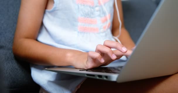 Menina com fones de ouvido usando laptop na sala de estar — Vídeo de Stock