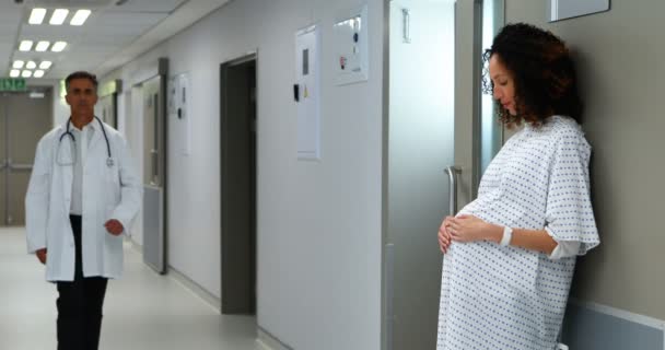 Pregnant woman touching her belly while doctor walking in corridor — Stock Video