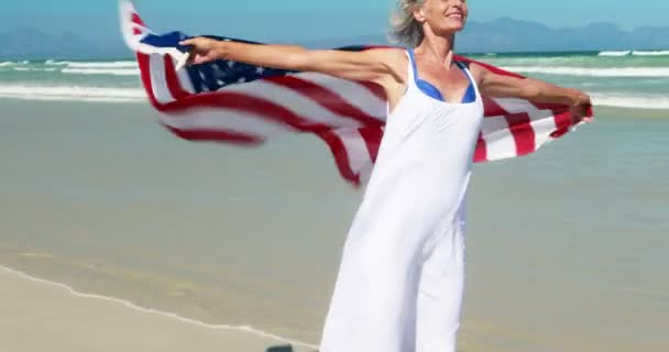 Mulher sênior com bandeira americana na praia — Vídeo de Stock