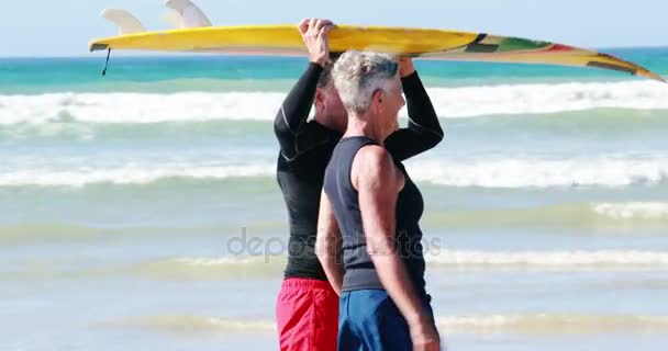 年长的夫妇在海滩上散步的时候，头顶携带冲浪板 — 图库视频影像