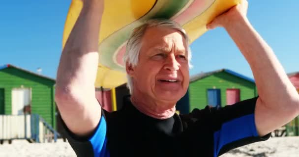 Hombre mayor en traje de neopreno llevando tabla de surf sobre la cabeza — Vídeos de Stock