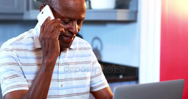 Homem sênior falando no telefone celular enquanto usa laptop — Vídeo de Stock